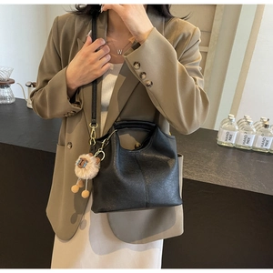 Detail of black leather crossbody bag with lychee texture and plush sheep charm on model