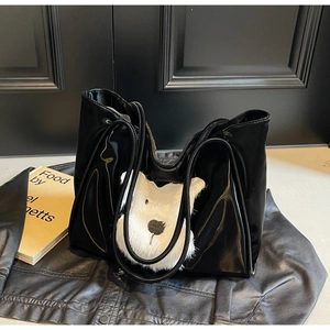 Glossy black tote bag with white plush bear decoration on a black leather background