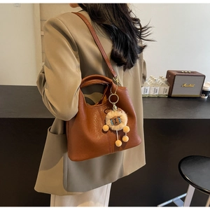 Close-up of brown litchi grain leather bucket bag with plush charm on a beige suit