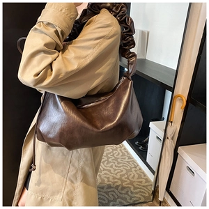 Détail du sac hobo marron foncé avec bandoulière plissée sur un trench-coat kaki