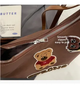 Close-up of a smooth silver metal zipper on a brown canvas tote bag with bear embroidery