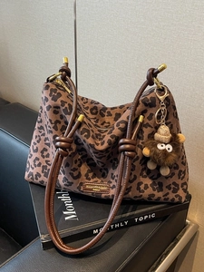 Large leopard print tote bag with brown leather straps and fuzzy monster charm accessory