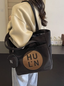 Large black canvas tote bag with brown logo patch and detachable mini round pouch