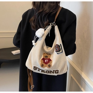 Detail of cream canvas hobo bag with teddy bear embroidery and brown leather strap