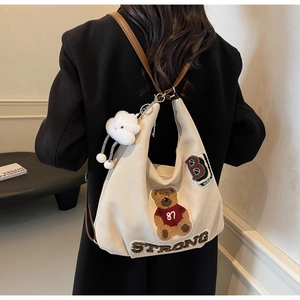 Detail of canvas hobo bag with teddy bear embroidery and brown leather strap on shoulder