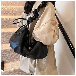 Détail du sac à bandoulière plissé noir avec bandoulière à volants sur escalier beige