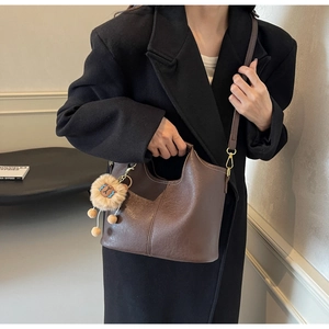 Deep brown leather tote bag with lion pendant and long strap shown on a black coat