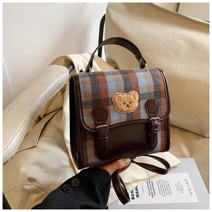 Detail of vintage plaid handbag featuring a plush bear motif and brown leather straps