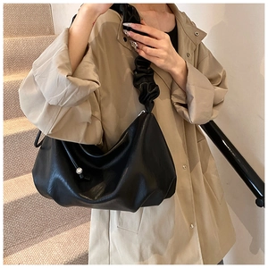 Détail du sac croissant plissé noir porté avec un trench beige pour un style élégant