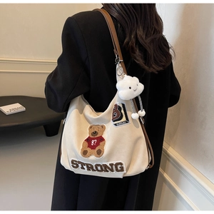 Detail of beige tote bag featuring teddy bear embroidery and a cute cloud charm
