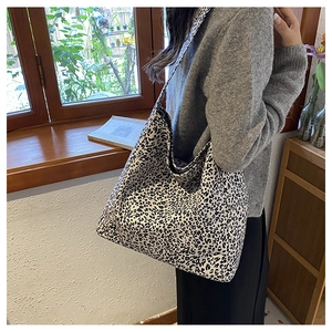 Detail of a large leopard print canvas tote bag carried by a model in a cozy interior setting