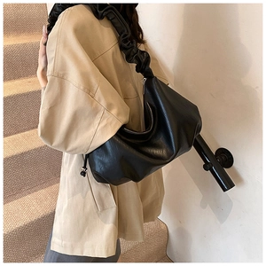 Détail d'un sac à bandoulière noir en croissant avec un design de sangle à volants