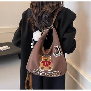 Detail view of brown nylon hobo bag with teddy bear embroidery and white plush charm