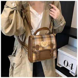 Detail of coffee plaid schoolbag with plush bear patch and leather buckle straps