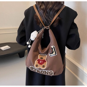 Detailed view of brown canvas tote with embroidered patches and plush rabbit charm