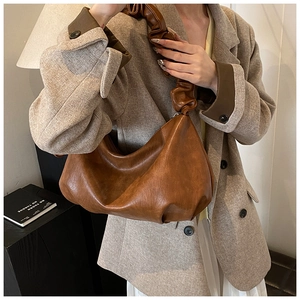 Détail d'un sac en demi-lune plissé marron montrant la texture du cuir brillant vintage