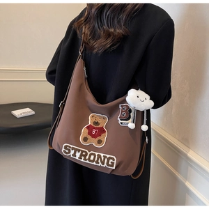 Detail of brown tote bag featuring bear embroidery and cloud plush charm on a model