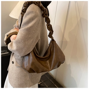 Gros plan d'un sac lune marron foncé avec bandoulière plissée sur un blazer beige