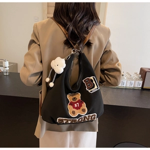 Close-up of black tote bag with bear embroidery, brown straps, and plush cloud charm