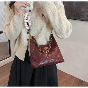 Modella che indossa una borsa a tracolla trapuntata bordeaux con catena d'oro e chiusura