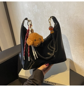 Detalle de bolso hobo negro brillante con asa de ámbar y colgante de perro peluche