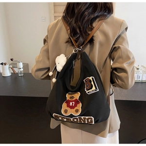 Close-up of black backpack with teddy bear embroidery and a white cloud charm detail