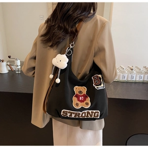 Detail of black canvas hobo bag with embroidered bear and plush cloud charm on model