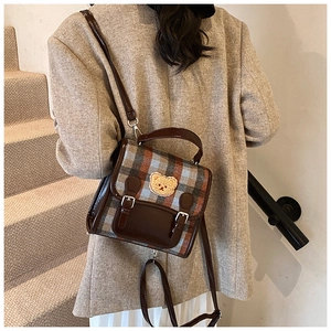 Detail of vintage plaid shoulder bag with cute bear patch worn by a model