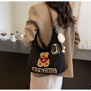 Detail of black tote bag with bear patch embroidery and brown leather strap on model