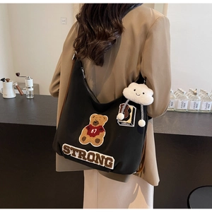 Detail of black canvas tote bag with teddy bear patch and cloud plush pendant