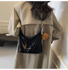 Bolso hobo de charol negro brillante con colgante de oso mostrado al hombro del modelo