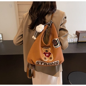 Close-up of brown canvas tote with bear embroidery, strong text and cloud charm