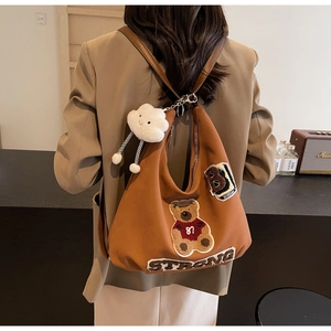 Detail of a brown tote bag featuring teddy bear varsity patches and a soft cloud charm