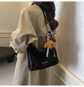 Detalle de bolso bandolera negro satinado con logo dorado y perro de peluche en gabardina