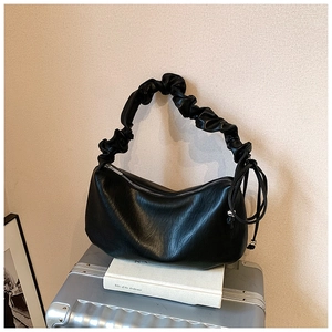 Détail de la poignée plissée noire du sac croissant en cuir posé sur une valise