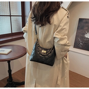 Dettaglio borsa hobo in pelle trapuntata nera con catena d'oro su un trench coat