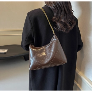 Détail d'un sac bandoulière matelassé marron foncé avec chaîne porté par un mannequin