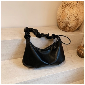 Détail du sac hobo en cuir noir froncé avec fermeture éclair argentée sur pierre