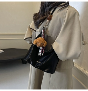 Detalle de bolso de cuero negro con colgante de peluche y correa decorada con cuentas