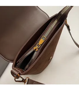 Detail of smooth gold zipper and metallic shoulder strap hook on brown leather bucket bag