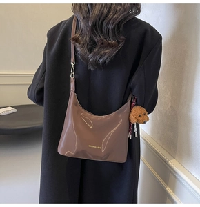 Bolso hobo de media luna marrón brillante con un tierno dije de osito de peluche al hombro