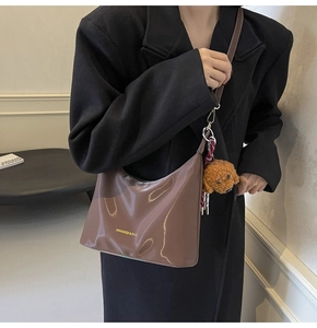Detalle de bolso tote de charol marrón con colgante de osito y pañuelo de seda a rayas