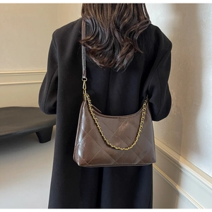 Détail d'un sac bandoulière marron foncé matelassé avec chaîne dorée sur un manteau noir