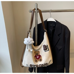Detail view of beige hobo bag with teddy bear embroidery and brown leather strap