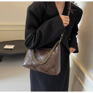 Détail de la texture matelassée et de la chaîne dorée sur le sac porté épaule marron