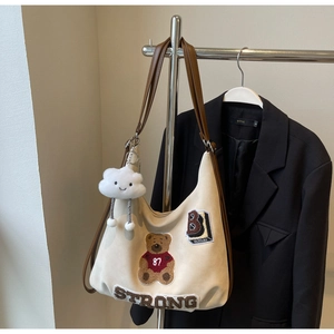 Detail view of cream canvas tote bag with bear embroidery and white cloud keychain charm