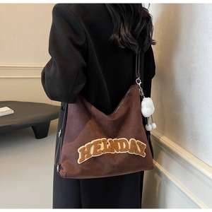 Détail d'un cabas en daim marron foncé avec lettres en peluche et pendentif pompon