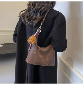 Detalle de bolso hobo de cuero marrón con correa de cuentas y colgante de peluche