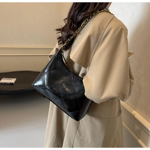 Détail du sac matelassé noir avec chaîne porté sur un trench-coat beige chic