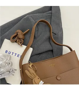 Detail of brown litchi pattern leather tote bag with a plush rabbit charm on a grey blazer